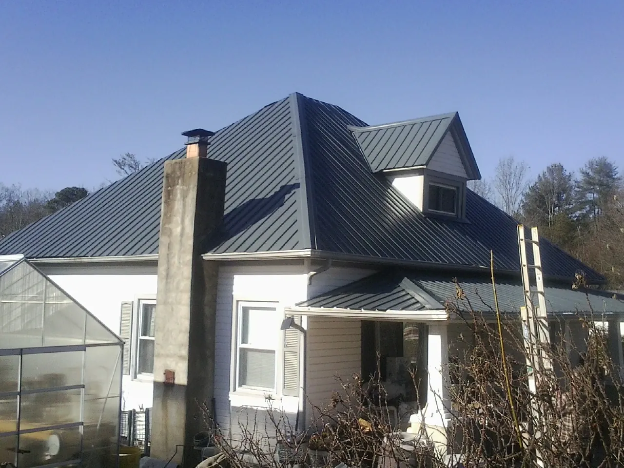 Dark blue standing seam metal roof on a white farmhouse with dormer — Slate & Tile Roof Repair by Roofing Brothers in Elberta