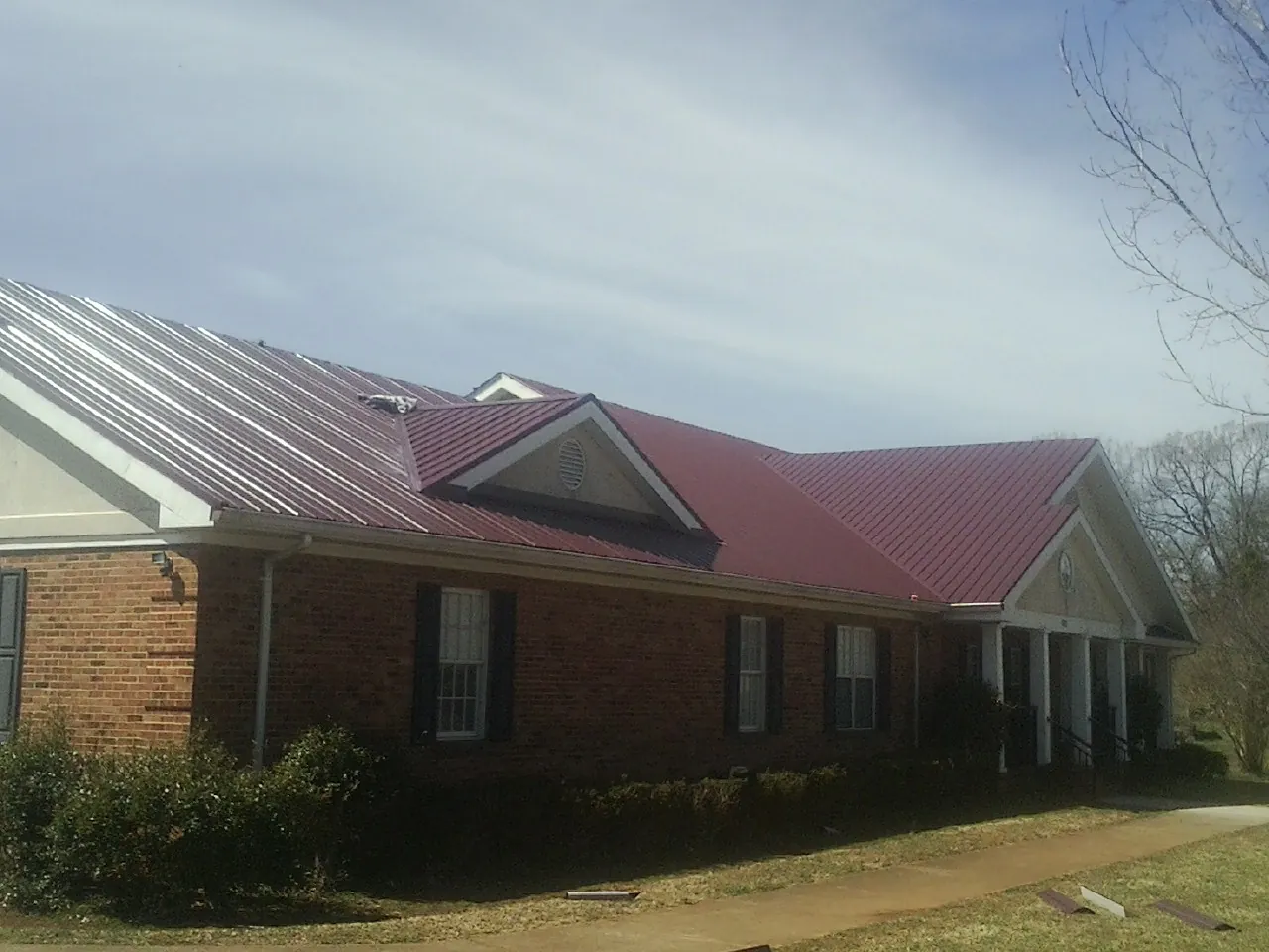 Red metal roof with gabled entries on a long brick building, from a Hail Damage Roof Repair job in Elberta