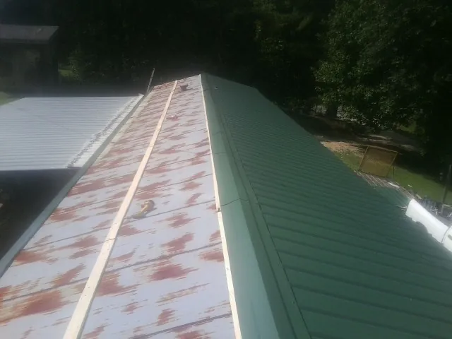 Old rusted panels beside newly installed green metal roofing — Wind Damage Roof Repair by Roofing Brothers in Elberta