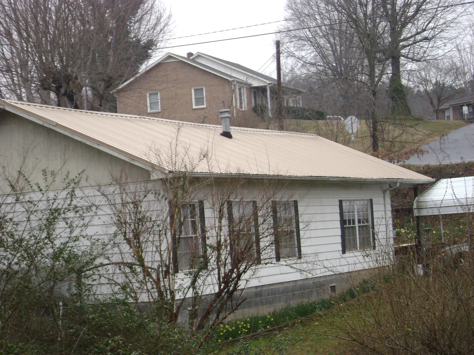Tan metal roof on a white sided house set into a hillside — Commercial Roofing by Roofing Brothers in Elberta